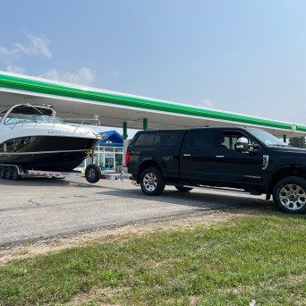 Truck towing a large boat at a gas station under a clear sky.