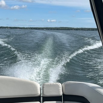 View from a boat showing water wake under a cloudy blue sky.