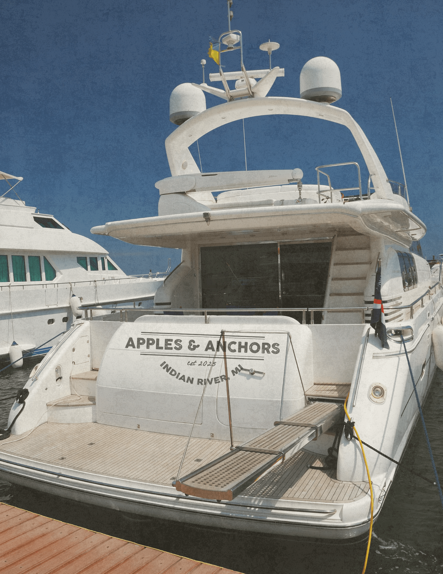 White yacht named 'Apples & Anchors' docked at a marina.