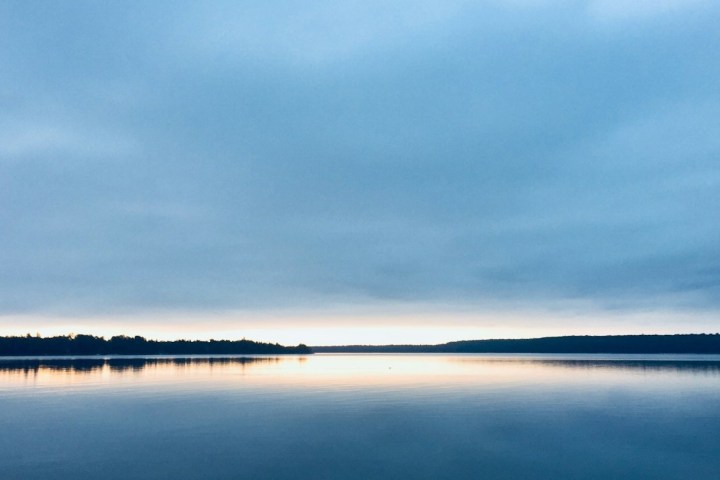 Calm lake with a cloudy sky and forests on both shores at dusk.