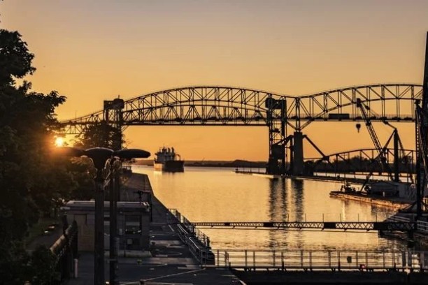 Sunset over canal with bridge and industrial structures.